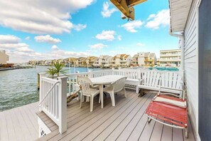 Een terras met een tafel en stoelen, een rode bank en uitzicht op een jachthaven met gebouwen.