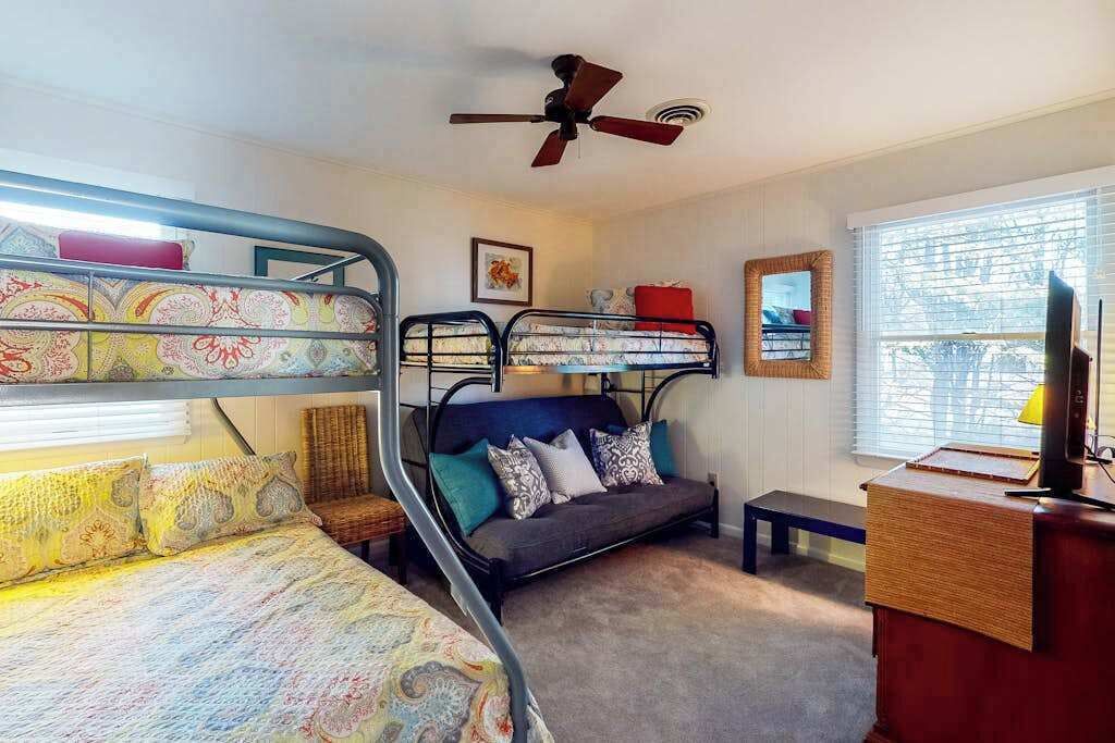 A room with bunk beds, a sofa, a desk, a television, and a ceiling fan.