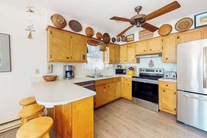 A kitchen with wooden cabinets, a central island, a stove, a microwave, and a refrigerator. - Canal-front home with boat dock, large deck, AC, washer/dryer & WiFi (Ocean City)