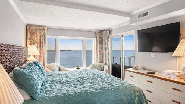 Ein Schlafzimmer mit Bett, Fernseher, Schreibtisch und Meerblick.