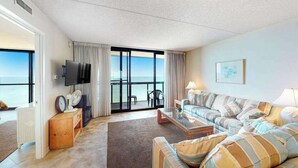 Un salon comprenant un ensemble de canapés, un téléviseur à écran plat, une table basse et une vue sur la mer grâce à de grandes fenêtres.