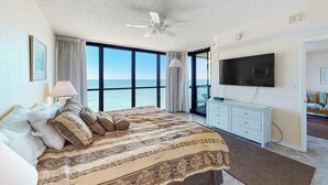 Une chambre avec un grand lit, un ventilateur de plafond, une télévision et une vue sur l’océan.