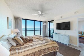 A bedroom with a large bed, a ceiling fan, a TV, and a view of the ocean. - Darling oceanfront condo with balcony, W/D, AC, pools & game room (Ocean City)