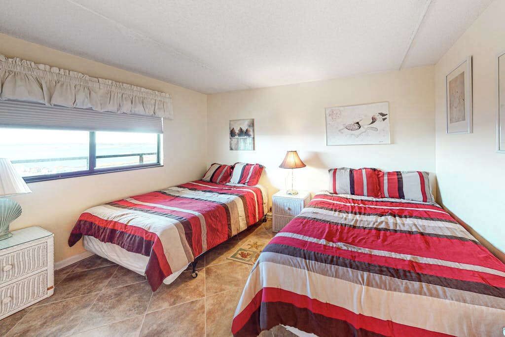 A bedroom with two beds, a window, a lamp, and artwork on the walls.