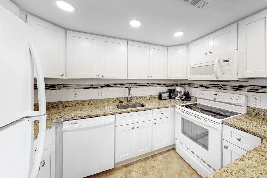 Una cocina moderna con armarios blancos, encimeras de granito, microondas integrado, estufa y lavavajillas.