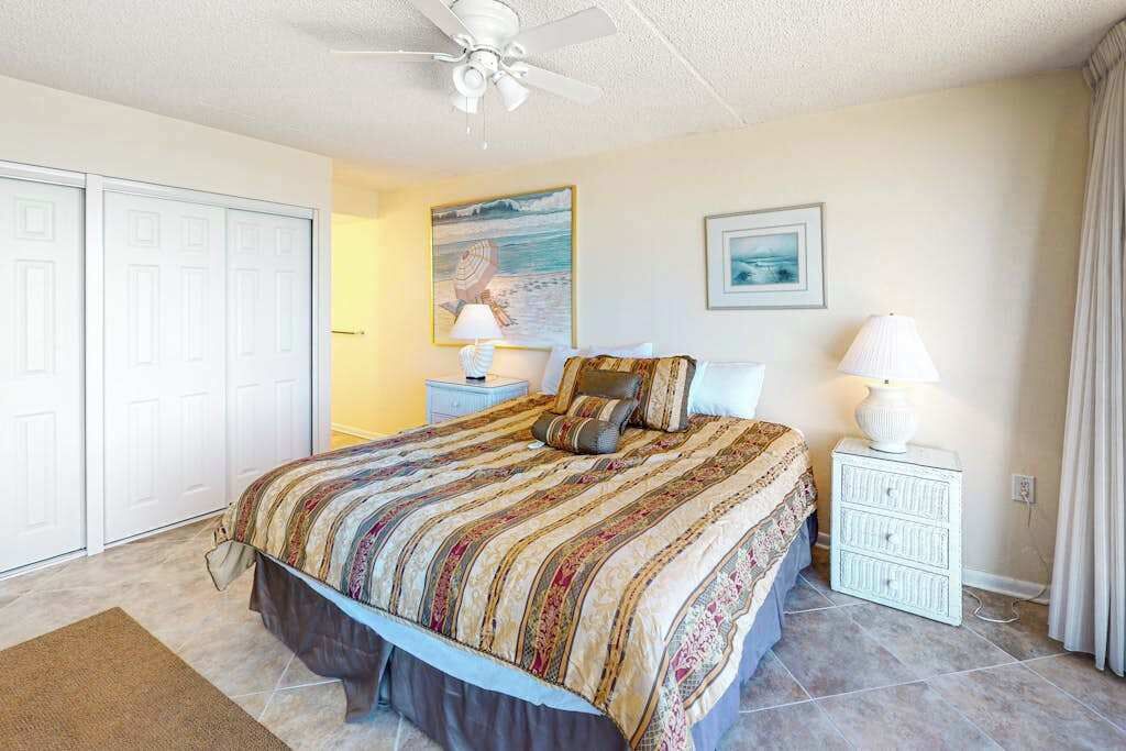 A bedroom with a bed, two bedside tables, a ceiling fan, and a door.