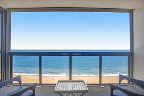 A balcony with a view of the beach, two wicker chairs, and a small table. - Beachfront condo with great views, balcony, pools & game room (Ocean City)