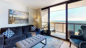 A modern hotel room with a large balcony, a sofa, a coffee table, and a painting. - Updated oceanfront condo with balcony, AC, W/D, pools & sauna (Ocean City)