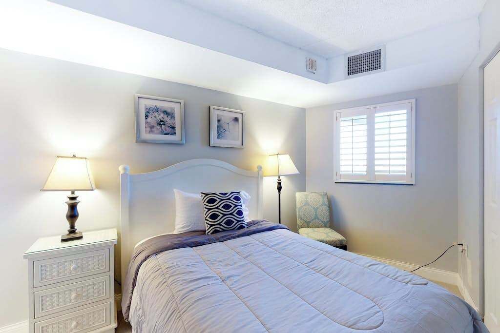 Quarto com cama, mesas de cabeceira, luminárias, uma cadeira e duas quadros na parede.