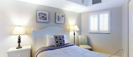 Quarto com cama, mesas de cabeceira, luminárias, uma cadeira e duas quadros na parede.