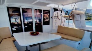 L’intérieur d’un bateau, avec une table, des sièges rembourrés et une vue sur l’eau à travers les fenêtres.
