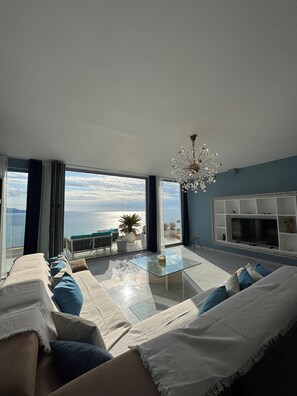 Una sala de estar con sofá, mesa de centro, televisor y vista al mar.