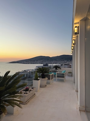 A balcony with outdoor furniture, potted plants, and a view of the sea and cityscape. - RIO Apartments Saranda 1 (Sarandë)