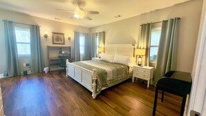 A bedroom with a bed, a desk, a chair, a nightstand, a lamp, and a ceiling fan.
