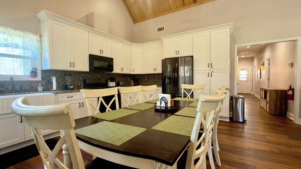 A modern kitchen with white cabinets, a central island, and a dining area with white chairs.
