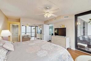 Un dormitorio con una cama grande, televisión, cómoda y puerta corrediza de vidrio que da a un balcón.