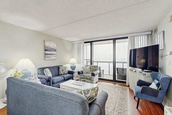 Sala de estar con sofá, sillones, una mesa de centro, televisor y balcón con vistas.