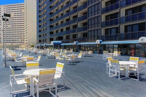 Une cour d’hôtel avec des espaces de repos en plein air, un immeuble à plusieurs étages doté de balcons et un ciel dégagé.