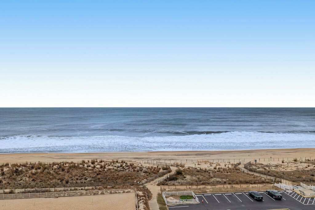 Blick auf einen Strand mit Parkplatz und einem eingezäunten Bereich.