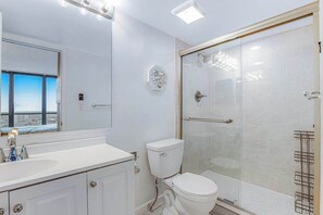 A bathroom with a glass shower enclosure, a white toilet, and a large mirror above the sink. - Convenient beachfront condo with angled views, cozy balcony, pools, gym & tennis (Ocean City)