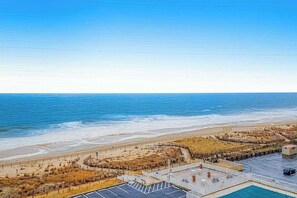 A coastal hotel with a parking lot, a pool, and a beach view. - Convenient beachfront condo with angled views, cozy balcony, pools, gym & tennis (Ocean City)