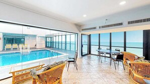 A spacious indoor area with a pool, wicker furniture, and large windows offering ocean views. - Updated condo with balcony, pools, gym, tennis court & AC (Ocean City)