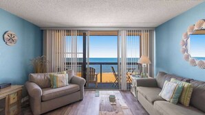 A room with two sofas, a coffee table, and a view of the beach through large windows. - Updated condo with balcony, pools, gym, tennis court & AC (Ocean City)