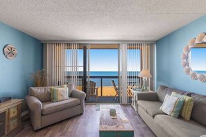 A room with two sofas, a coffee table, and a view of the beach through large windows. - Updated condo with balcony, pools, gym, tennis court & AC (Ocean City)