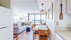 A modern interior with a dining area, sofa, and large windows. - Budget-friendly beachfront studio with balcony, tennis, gym, pools & sauna (Ocean City)