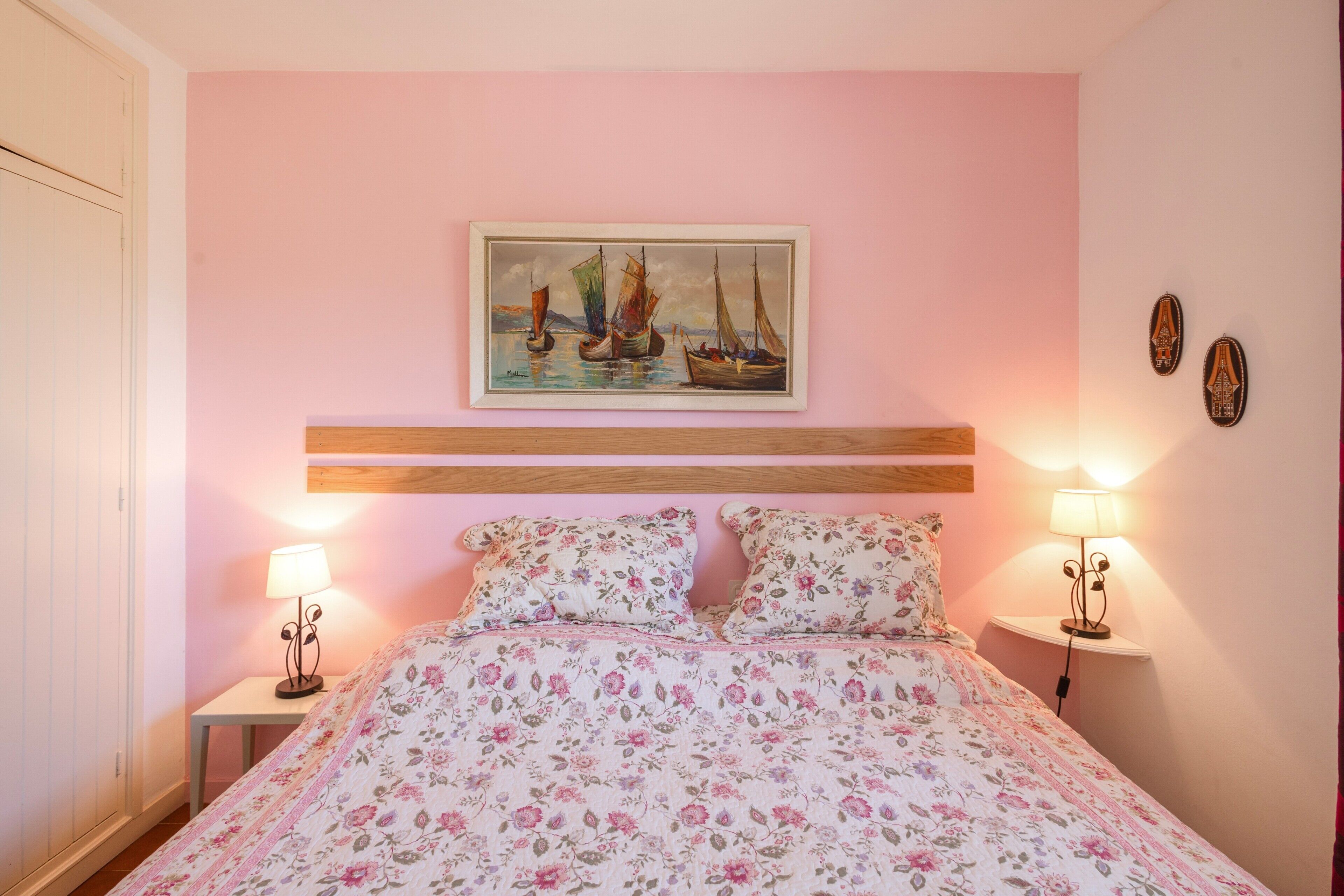 Un dormitorio con una cama, dos lámparas de noche, un cuadro de barcos de vela y un cabecero de madera.