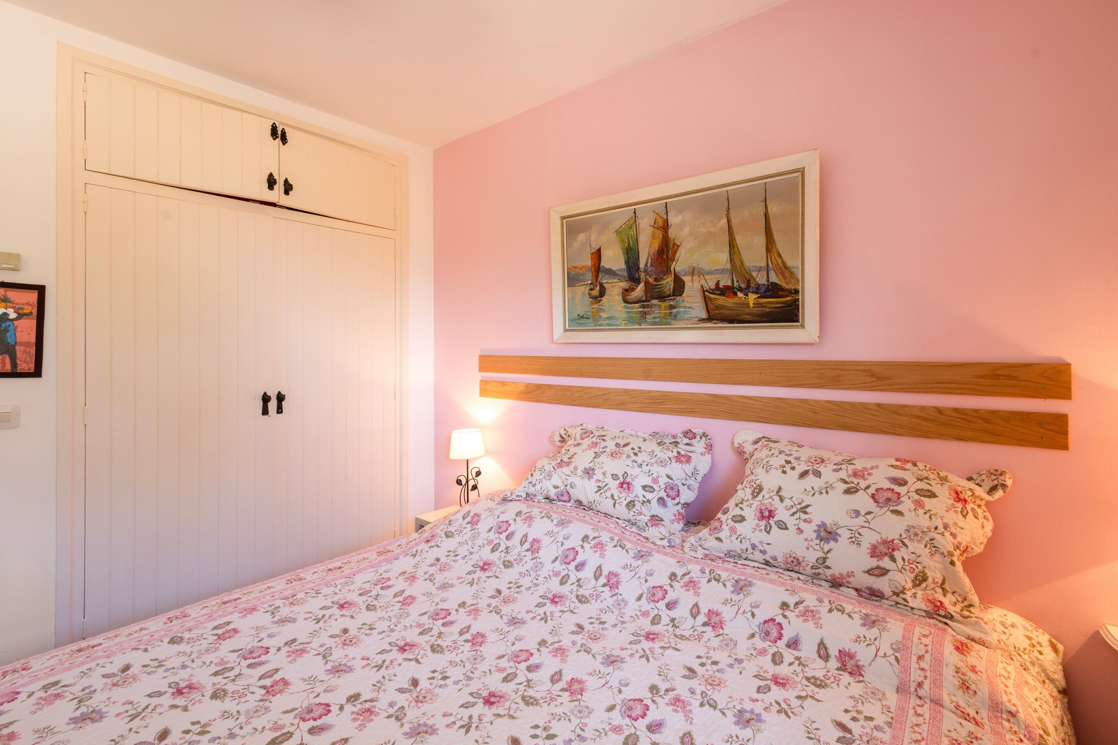 A bedroom with a bed, a painting, a wardrobe, and a nightstand.