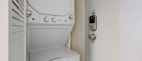 Lavadora blanca con perillas de control y pantalla digital, fijada a la pared junto a una puerta con cerradura.