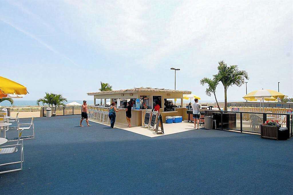Um bar no terraço com mesas ao ar livre, área de serviço de alimentos e palmeiras.