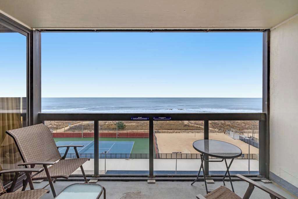 Un balcon avec vue sur l’océan, un court de tennis et une plage.