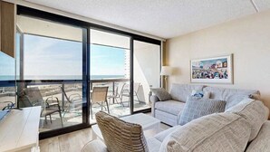 Una sala de estar moderna con un gran ventanal corredizo que da a un balcón, un sofá, una mesa de centro y un escritorio con una silla.