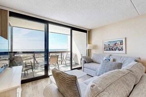 Ein modernes Wohnzimmer mit einem großen Schiebeglastür, die auf einen Balkon führt, einer Couch, einem Couchtisch und einem Schreibtisch mit Stuhl.