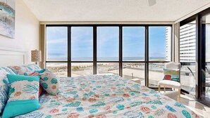 Un dormitorio con un ventanal grande, una cama con ropa de cama floral, una silla y vista a la ciudad.