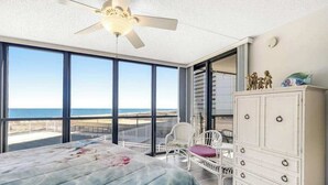 A bedroom with a bed, a dresser, a chair, and a view of the ocean.