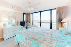 A bedroom with a bed, a television, a ceiling fan, a dresser, and a large window with a view. - Oceanfront condo with balcony, washer/dryer, pools, & gym (Ocean City)