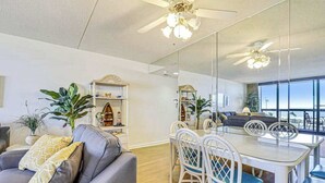 Un salon moderne comprenant un canapé, une table à manger, des chaises, des ventilateurs de plafond et une grande fenêtre.