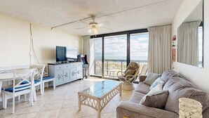 Una sala de estar con sofá, una mesa de centro de vidrio, una mesa de comedor con sillas, televisor y un balcón con vistas.