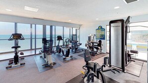 Un gimnasio con diverso equipo de ejercicio, ventanas amplias y vista al océano.