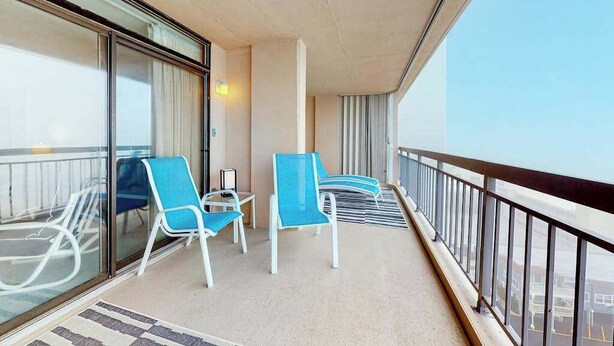 Een balkon met glazen deuren, twee blauwe stoelen, een klein tafeltje en uitzicht op de stad.