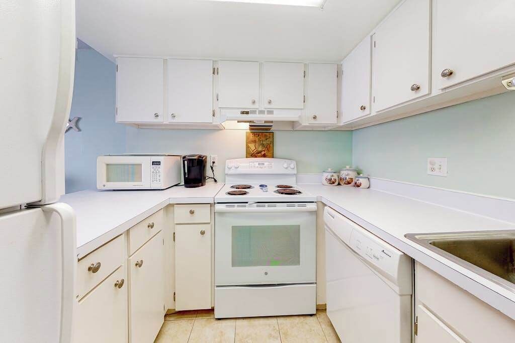 Cocina compacta con armarios blancos, estufa, microondas y lavavajillas.