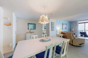A hotel room with a dining table, chairs, a sofa, a lamp, and a view of the sea. - Fountainhead Towers 1105 (Ocean City)