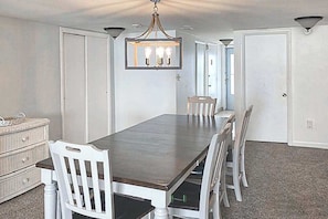 Ein Esszimmer mit langem Tisch, weißen Stühlen, einer Chandelier und einem Teppichboden.