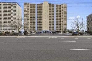Ein mehrstöckiges Hotel mit zentralem Eingang, einem Parkplatz und einem von Bäumen gesäumten, eingezäunten Bereich.
