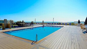 En pool med ett trädäck, solstolar och utsikt över havet.