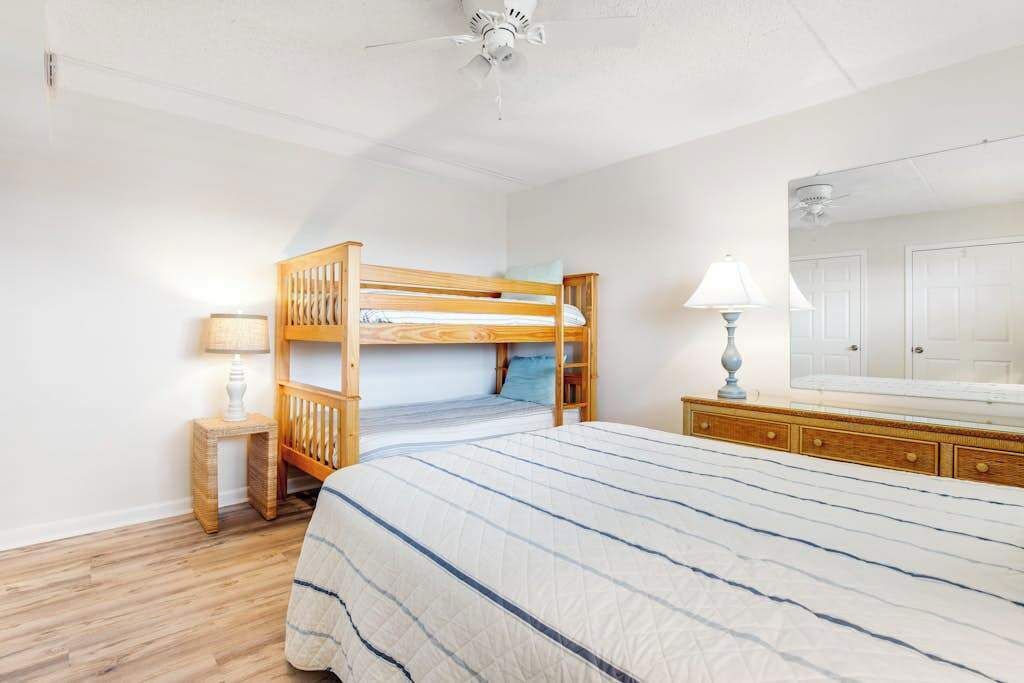 Ein Schlafzimmer mit einem Etagenbett, einem Nachttisch mit Lampe, einer Kommode und einem Spiegel.