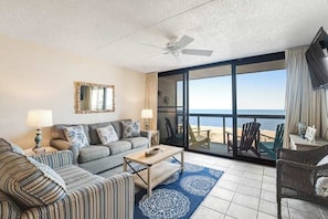 A living room with a sofa, a coffee table, a TV, and a view of the ocean. - Splendid beachfront condo with balcony, views, pool, gym, tennis, AC & sauna (Ocean City)